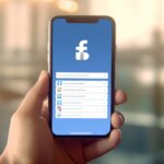 Телефон в руке с логотипом facebook на экране