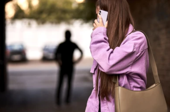 Hier ist das Bild einer Frau am Telefon, die von einem Schatten in etwas, das wie eine Gasse aussieht, verfolgt wird