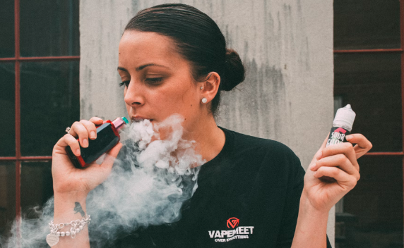 Gambar ini menunjukkan seorang wanita yang sedang melakukan vaping di udara terbuka